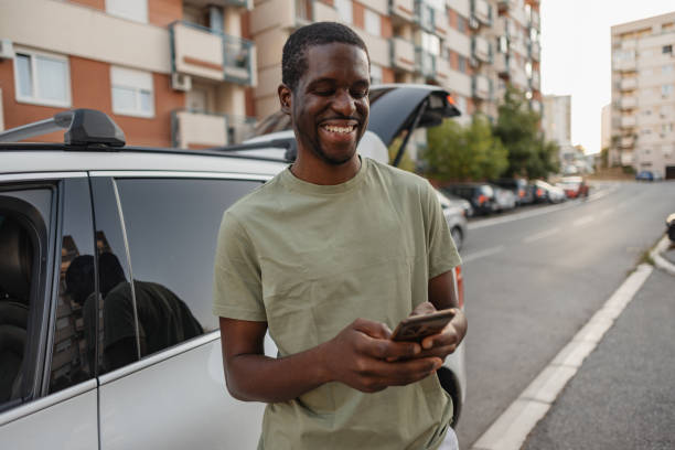 istock Man smiling at phone, standing near a white vehicle 2184765016