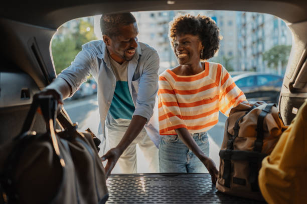 Couple loading luggage into car in urban setting.