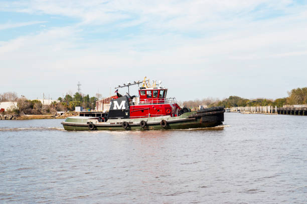 Savannah, Georgia, USA - 20 February 2024: A red tugboat operates on peaceful waters under a bright blue sky, approaching a docked location.