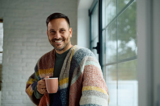 istock Happy man with cup of tea standing by the window and looking at camera. 2184770247