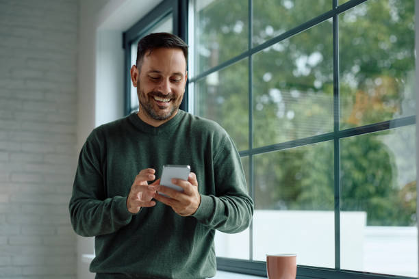 istock Happy man text messaging on mobile phone by the window. 2184770250