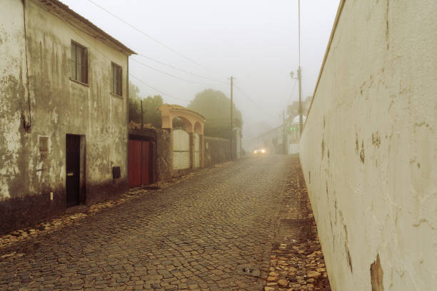 istock empty village cobbled street in the mist with an approaching vehicle 2184778468
