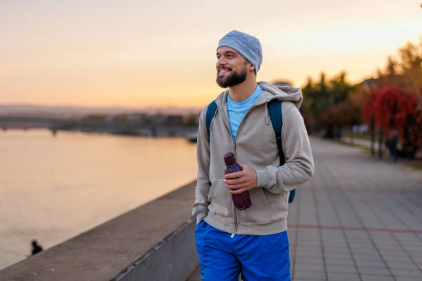 Man walking by riverside during sunrise with water bottle held