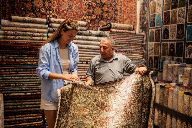 Mature Turkish male store owner showing a traditional Turkish carpet to a woman customer in his carpet store in Istanbul, Turkey.