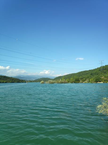 istock Serene lake surrounded by green hills under clear sky 2184784817