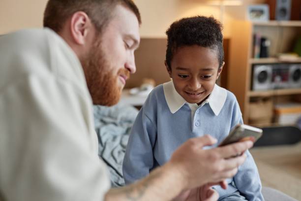 istock Happy Adopted Kid Using Phone with Dad while Having Fun Together in Kids Room 2184789200