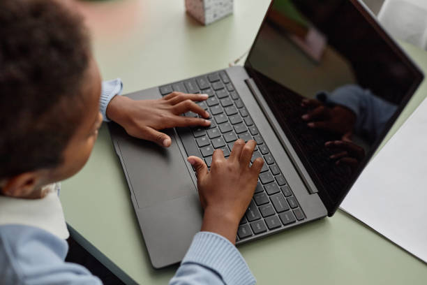 istock Hands of Black Boy Typing on Laptop Keyboard while Studying at Table in Kids Room 2184789226