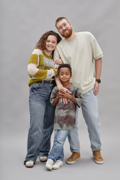 Smiling Adoptive Mother and Father with Son Looking at Camera on Gray in Studio