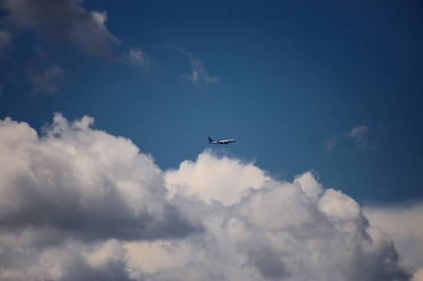 A commercial airplane is flying gracefully through a vast, cloudy blue sky, surrounded by fluffy cumulus clouds drifting by