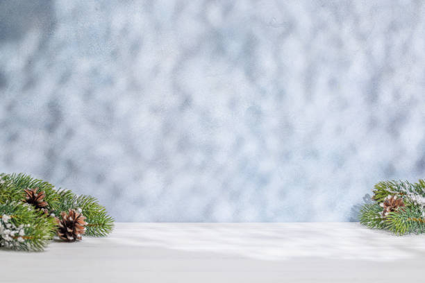 istock Christmas template featuring snowy fir tree branches on a table with shadows and sun glares softly falling on the wall 2184789539