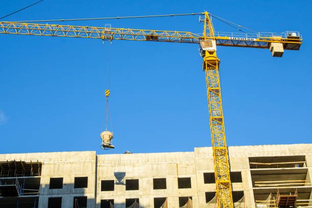 A LIEBHERR tower crane carries a load at a construction site. A special container contains liquid cement for pouring the walls of a monolithic residential building.