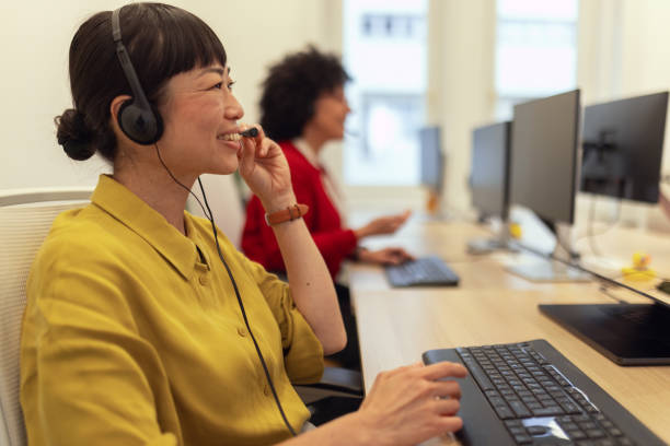 istock Two multiracial women work together in a call center. They sit side by side, each using their own computer and headphones for online consultations with clients 2184792670