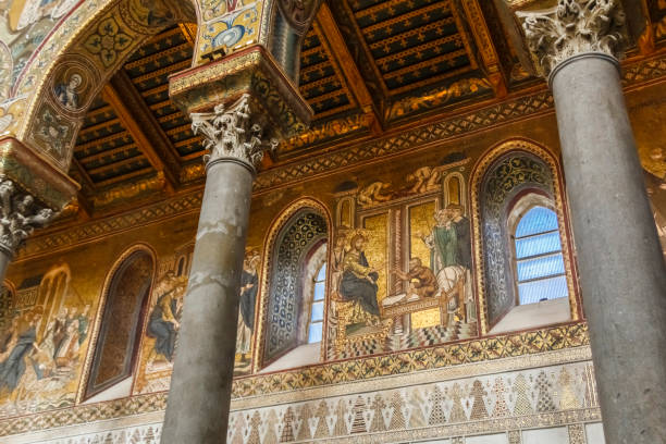 This close-up photograph reveals a breathtaking detail of Monreale Cathedral's interior, where intricate golden mosaics shine with vivid colors and complex designs. The image captures a section of the apse, adorned with shimmering Byzantine art depicting saints and religious symbols. The gold tesserae reflect the light, creating a warm, sacred glow that enhances the majestic ambiance of this architectural masterpiece.