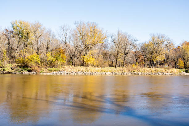 A river bank landscape in autumn with reflections in the water and blue sky background.