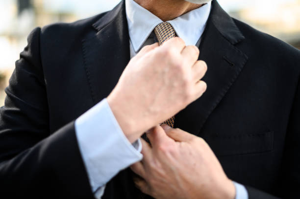 Confident businessman buttoning or adjust classic blue suit near window in hotel room at the morning. Handsome man wearing a nice suit on wedding day.