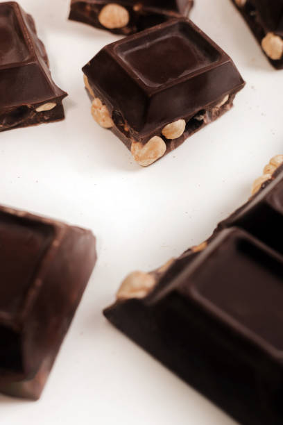 istock broken dark chocolate bar with hazelnuts on white backdrop, glowy golden background.top view of luxury desert, slabs one over another.empty space for text on box. 2184803513