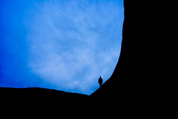 Hiker Silhouetted on Rock Rim - Desert hiker at dusk blue hour outlined against blue moody sky.