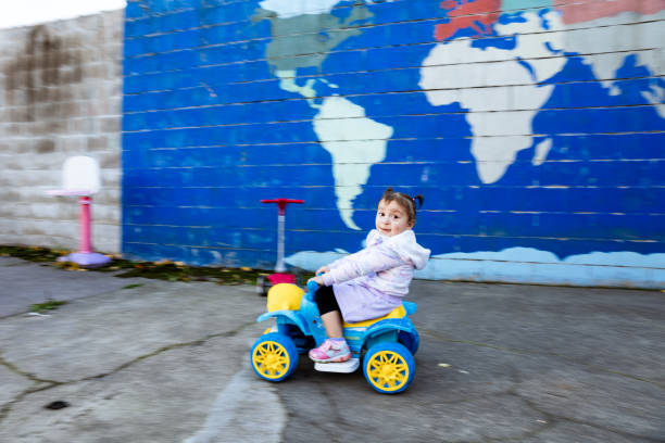 Happy hispanic girls (kindergarten aged) playing in their yard in the fall season. They are playing with toys and exploring their front and back yards as the leafs change colors. *Backyard Mural painted by photographer.*