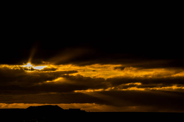 The sun is shining through the clouds, creating a beautiful and serene scene. The sky is dark and the clouds are thick, giving the impression of a storm brewing