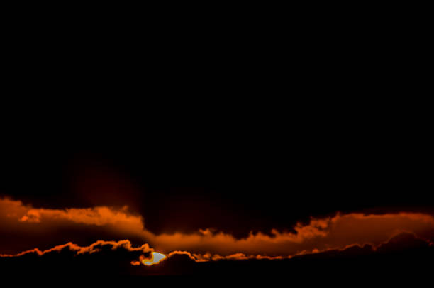 A black sky with orange clouds and a sun in the sky. The sky is dark and the sun is setting
