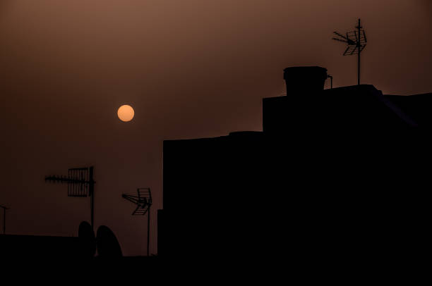 A silhouette of a building with a sun in the sky. The sun is setting and the sky is orange