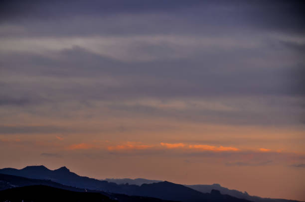 The sky is a beautiful orange color as the sun sets. The mountains in the background are covered in snow