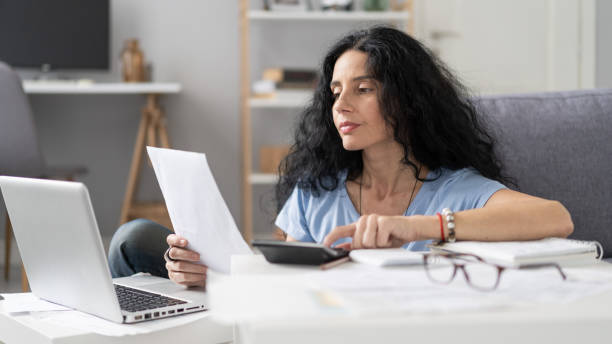 istock Thoughtful woman using a calculator and reviewing documents at a modern home workspace. 2184810339