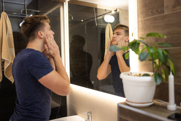 istock Young Man Applying Skincare Product in Modern Bathroom Mirror 2184814525