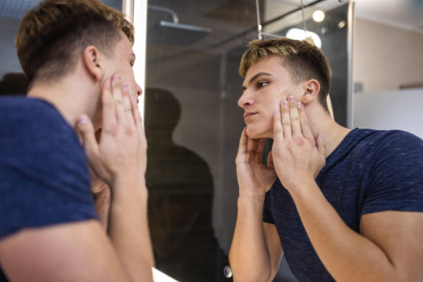 istock Young Man Examining Skin in Bathroom Mirror 2184814529