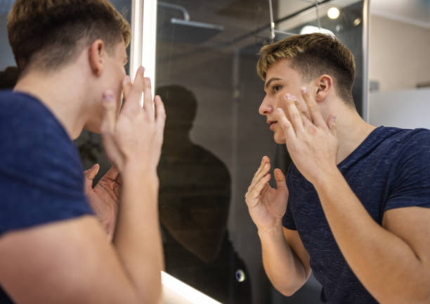 istock Young Man Examining Skin in Bathroom Mirror 2184814535