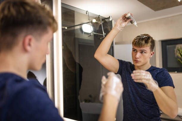 Young Man Applying Hair Dye in Modern Bathroom Mirror
