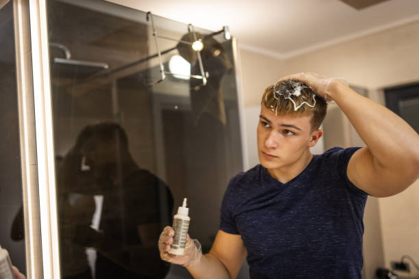 Young Man Applying Hair Dye in Modern Bathroom Mirror