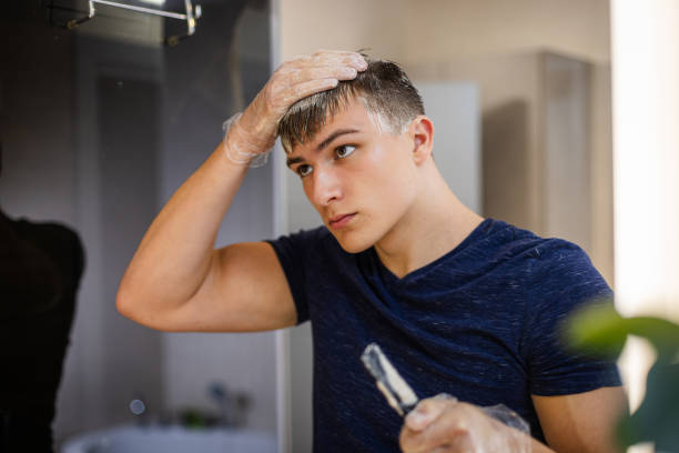 istock Young Man Dyeing Hair at Home in Front of Mirror 2184814549