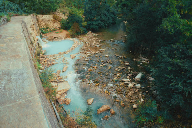 A tranquil image of sulfurous thermal waters cascading through a lush forest. The bright turquoise hue of the water, caused by its high sulfur content, contrasts beautifully with the earthy rocks and the surrounding greenery. Captured with a wide-angle lens, the photo exhibits a balanced composition and excellent dynamic range, emphasizing the unique color and textures of the landscape. The cascading thermal waters, surrounded by natural elements, evoke a sense of peace and rejuvenation.