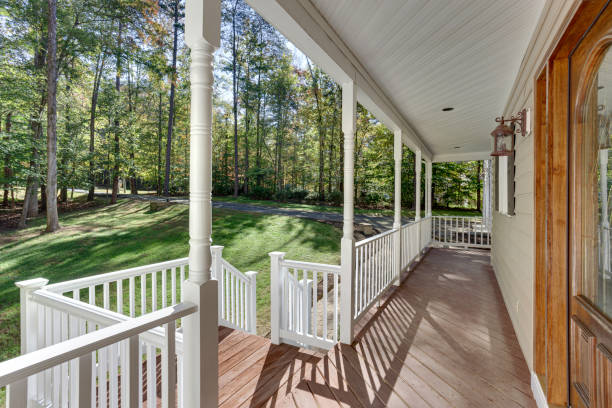 A charming covered porch features classic white railings and overlooks a beautifully wooded area, offering a tranquil retreat to enjoy the surrounding natural landscape.