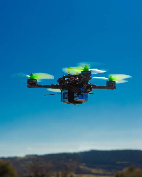 Weston Super Mare, United Kingdom – April 16, 2024: A self-built DIY FPV drone with green propellers flying against a clear blue sky with a scenic landscape in the background.