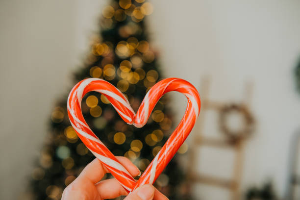 istock Hand holding a heart-shaped candy cane in front of a Christmas tree 2184840629