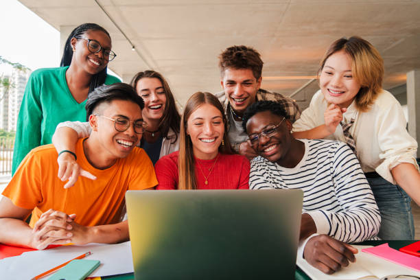 istock Big group of young students using a laptop to do the homeworks at high school library. Teenagers e-learning with a computer at university campus. Classmates talking and studying for a exam at class 2184849077