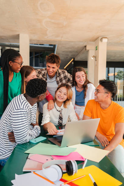 istock Vertical. Big group of real teenage students searching information using a laptop at university campus library. Multiracial smart classmates doing the homework task and studying the lesson for a exam 2184849722