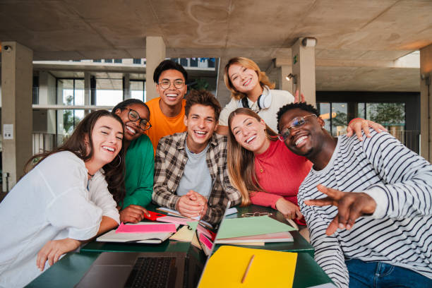 istock Happy young university students smiling and looking at camera enjoying together sitting in the library or classroom. Multiracial teenage friends laughing on a study break at campus. High school people 2184850383