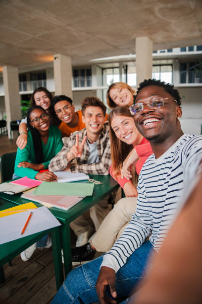 istock Happy young students taking a vertical selfie portrait together at university library. African american guy shooting a photo with his smiley classmates on a high school meeting. Friends at academy 2184850898