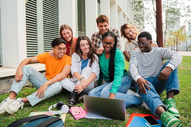 istock Portrait of multiracial college students using a laptop computer while having fun watching funny movie sitting on lawn after doing homework outside university campus. Smiling friends taking a break. 2184851258