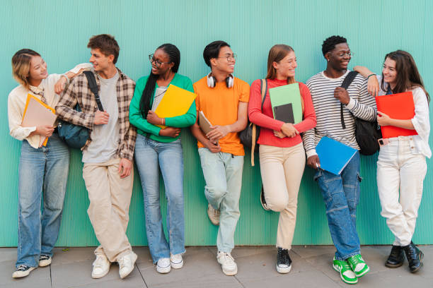 istock Diverse Group of College or High School Students Share Cheerful Moments Between Classes, Carrying Colorful Folders and Backpacks While Leaning Against Vibrant Teal Wall, Teenage Classmates talking 2184852872