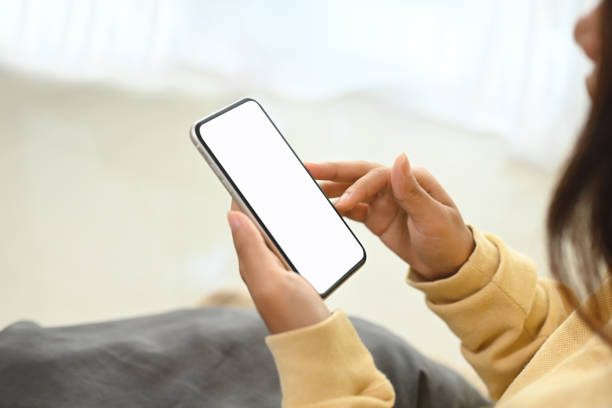 istock Woman in yellow sweater holding smartphone with white empty display sitting on sofa 2184864919