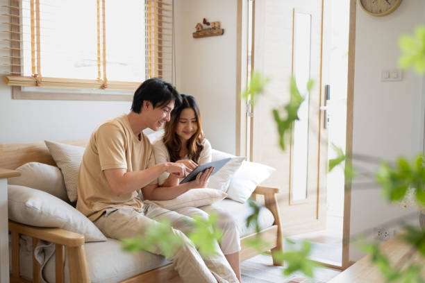 Relaxed asian couple using a digital tablet while relaxing together on sofa at home. stock photo