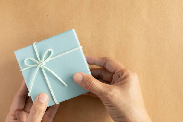 istock Hand of green gift box over brown background. Top view, flat lay with copy space. Concept for happy birthday, thank you, congratulations, Mother's day, anniversary, Valentine's day. 2184885661