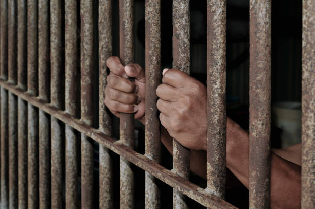 istock Hands of a prisoner behind prison bars on black background 2184889934
