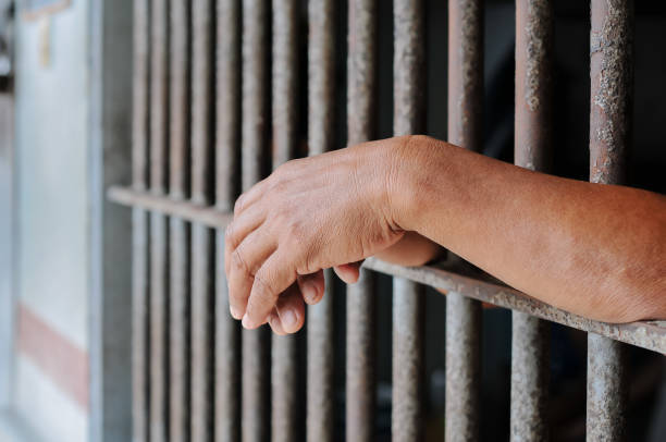 istock Hands of a prisoner behind prison bars on black background 2184889941