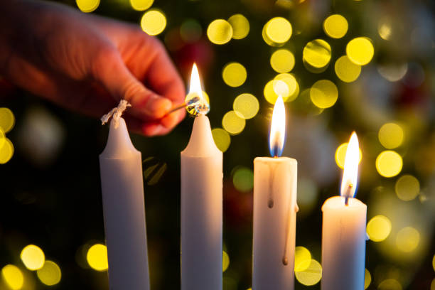 istock Hand lighting third candle with a match on Advent wreath with four pillar candles. Christmas tree with twinkling lights 2184890476