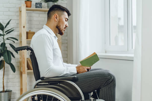 istock Disabled man in wheelchair reading a book indoors 2184891265